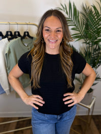 Woman wearing a short sleeve black top and blue jeans standing in a clothing store.