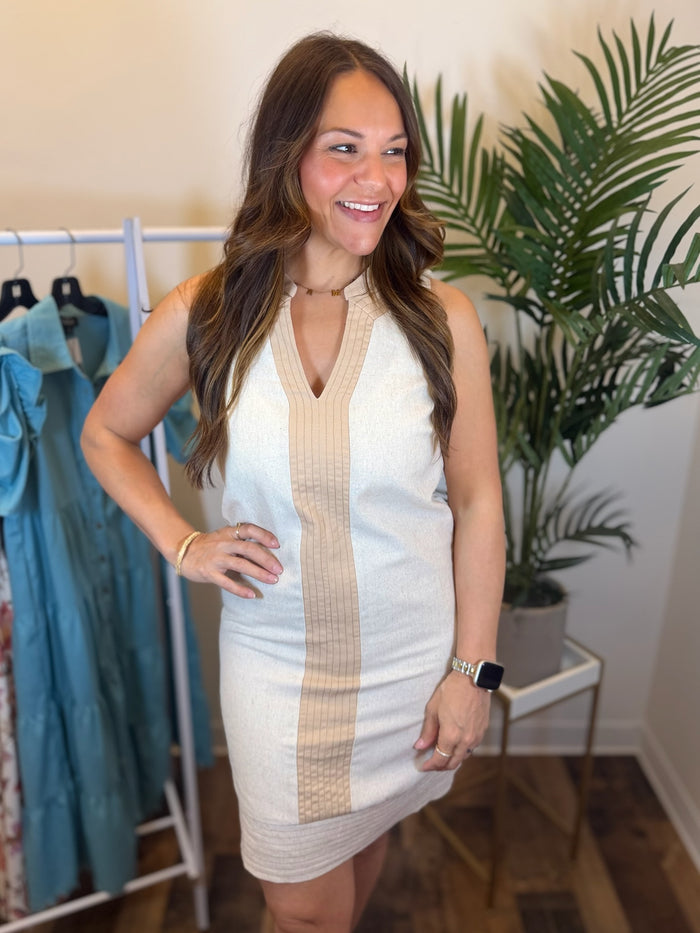 Woman wearing a sleeveless cream dress with beige accents in a clothing store.