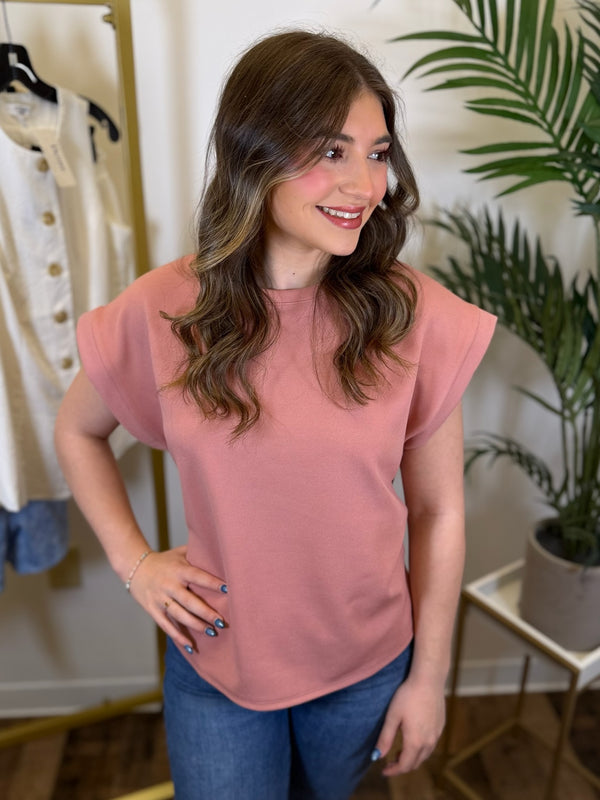 Woman wearing a pink short sleeve top and blue jeans in a store setting with plants.