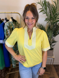 Woman wearing a yellow blouse with a striped collar in a clothing store.