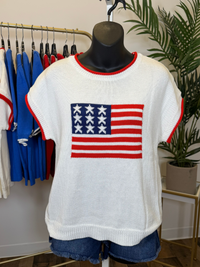 White short sleeve sweater with American flag design and red trim on a mannequin in a store setting.