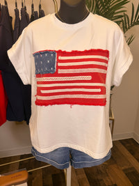 White t-shirt with American flag applique on a mannequin in a store setting.