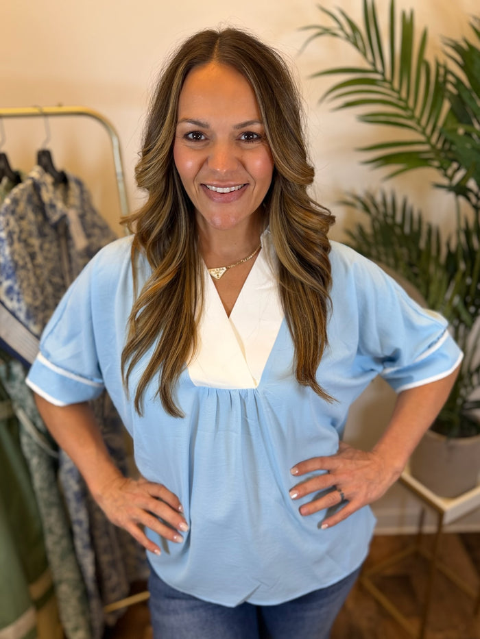 Woman wearing a light blue blouse with short sleeves and a white collar in a clothing store.