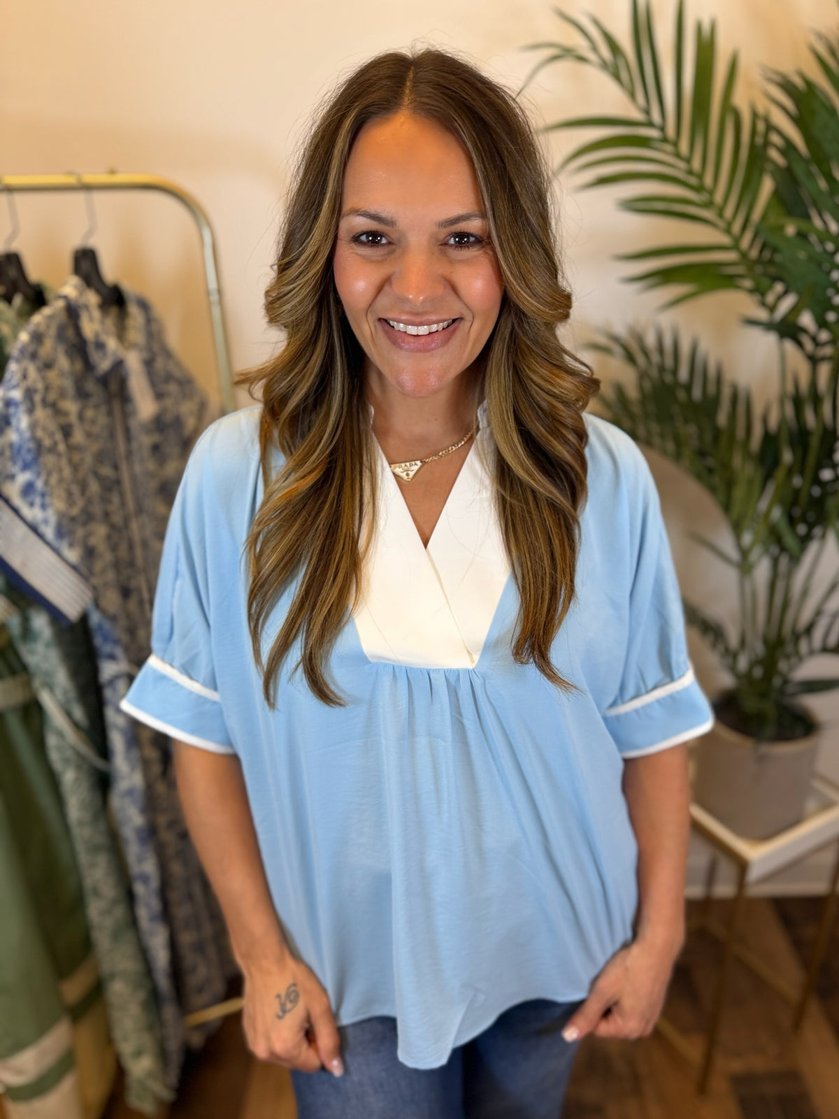 Woman wearing a short sleeve light blue blouse with white trim in a clothing store.
