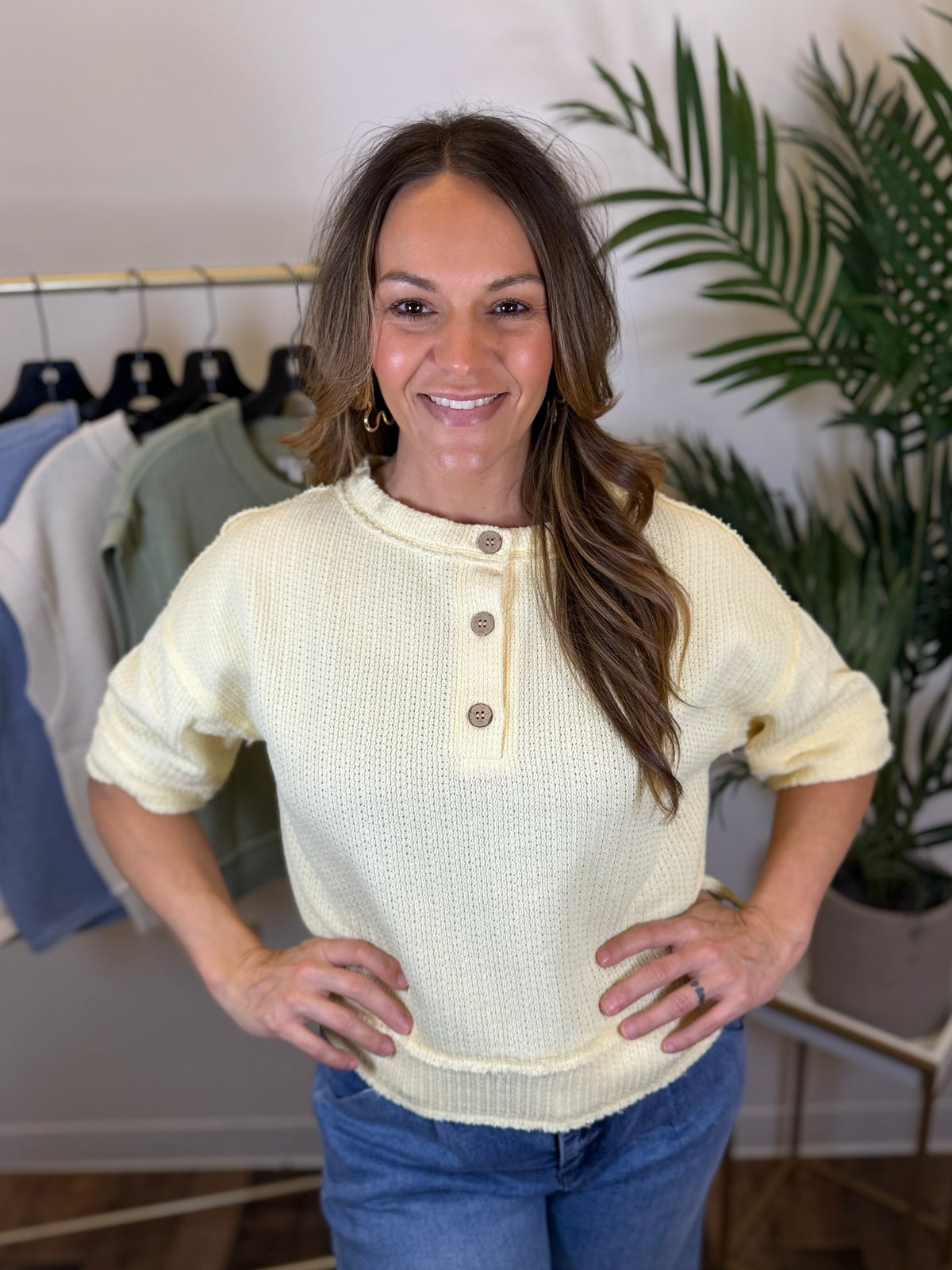 Woman wearing a butter-colored short sleeve sweater with buttons, standing in a clothing store.
