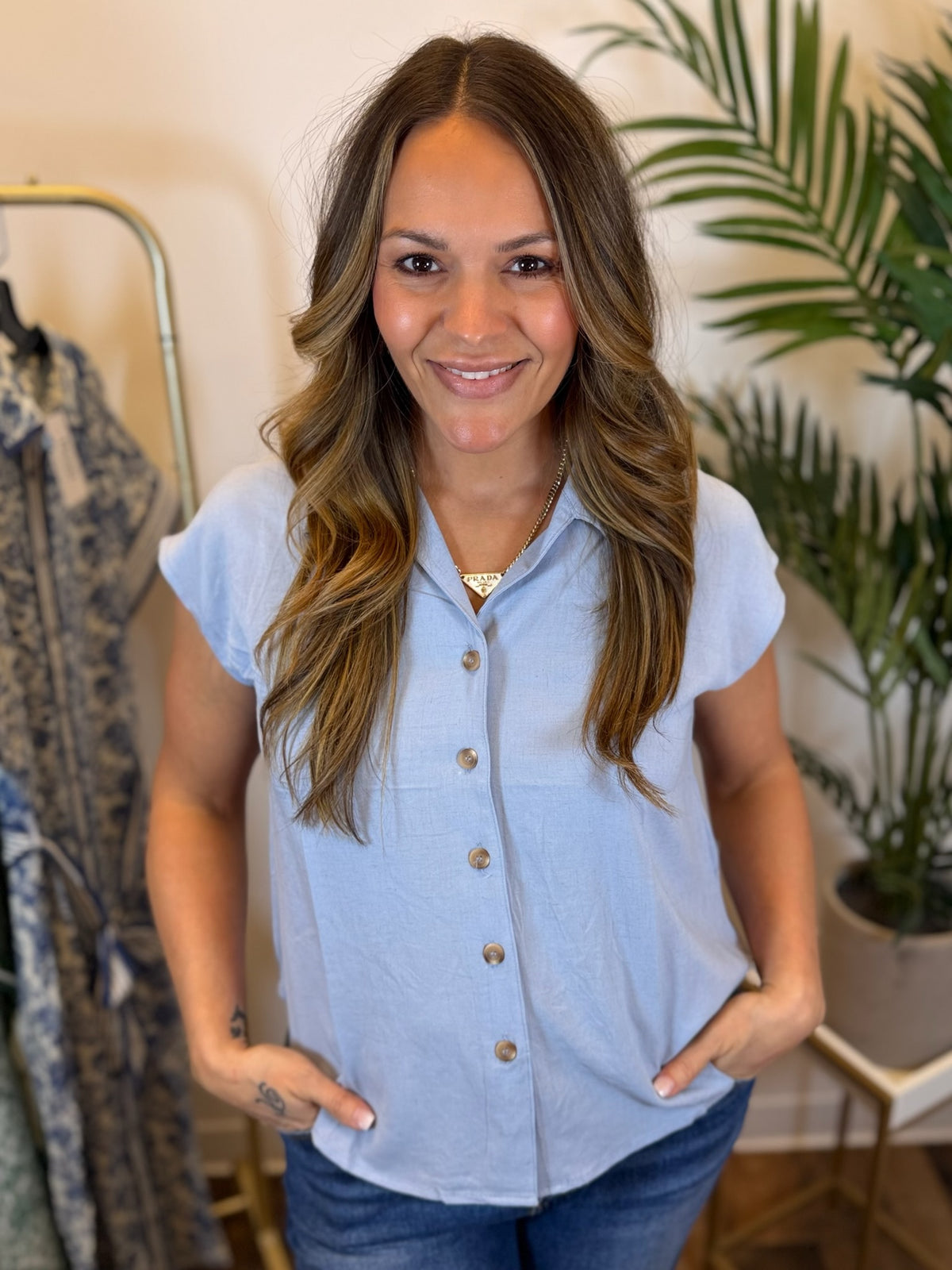 Woman wearing a light blue short sleeve button-up shirt in a clothing store setting.