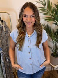 Woman wearing a light blue short sleeve button-up shirt in a clothing store setting.