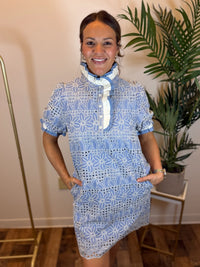 Woman wearing a blue and white floral dress standing indoors with a plant in the background