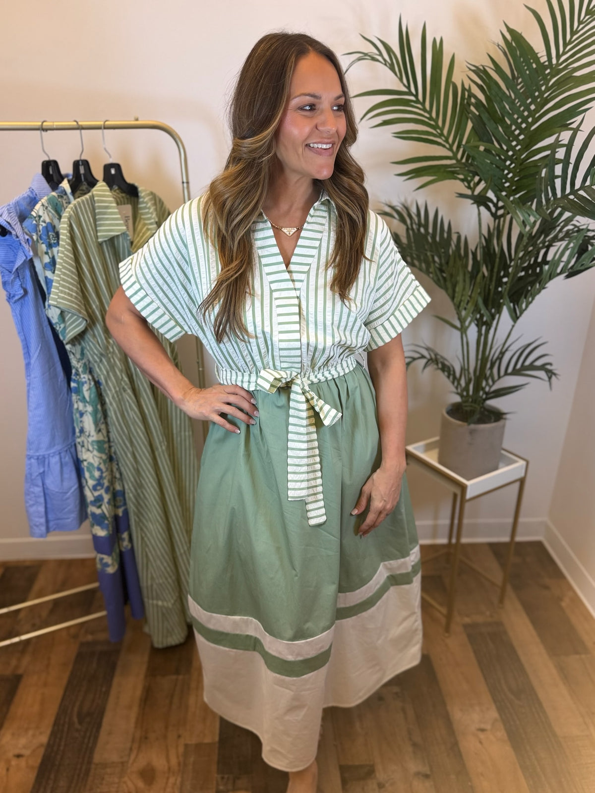 Woman wearing a sage and white mixed print dress with short sleeves and v neckline in a clothing store.