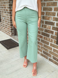 Person wearing light green pants and a white top against a brick wall.