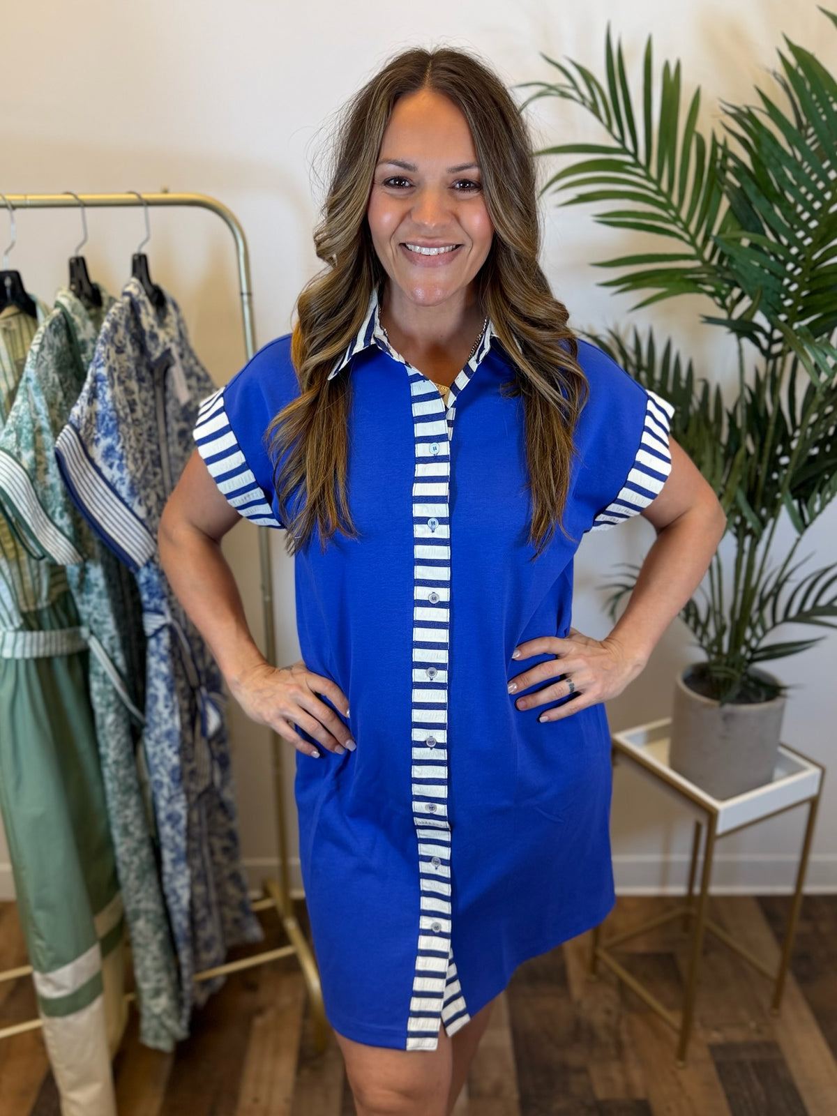 Woman wearing a blue button front dress with white stripes in a clothing store.