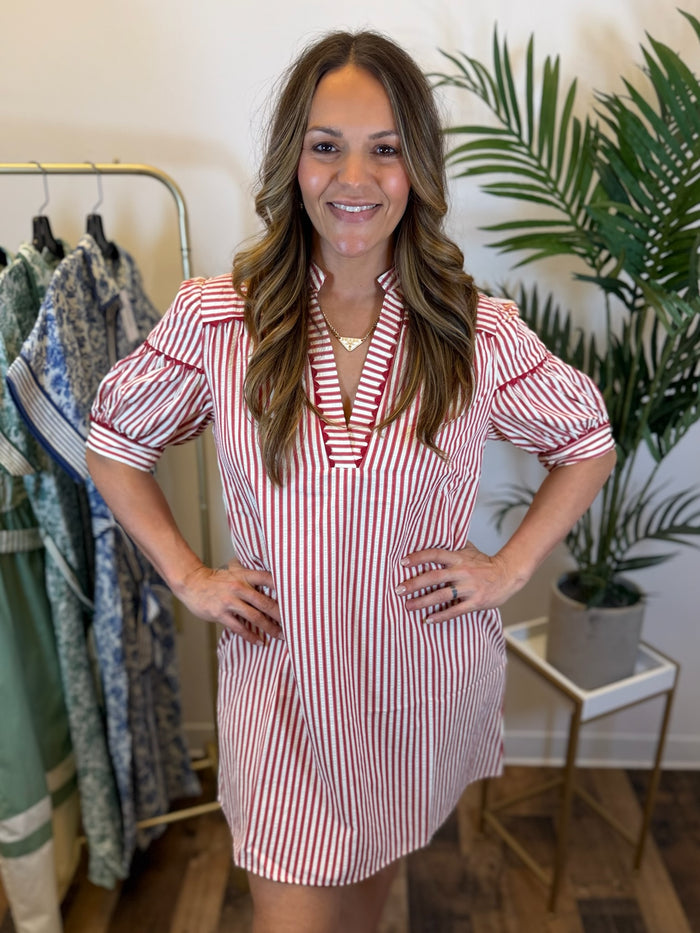 Woman wearing a short red and white striped dress with a split neckline and red trim details in a clothing store.