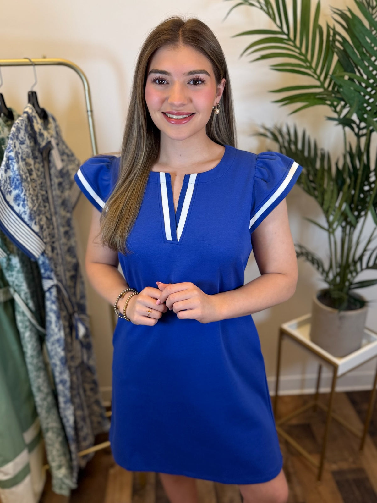 Woman posing in a royal blue v neck dress with ruffled cap sleeves and contrast trim details.