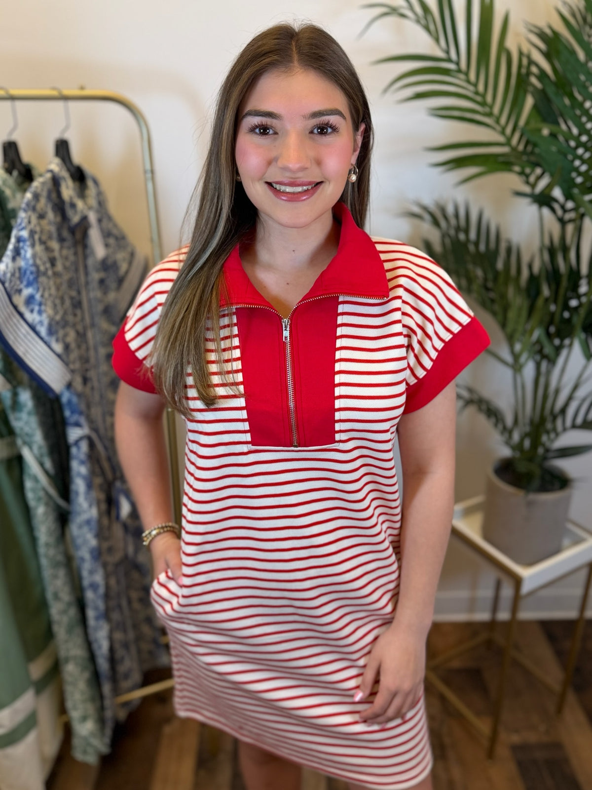 Woman wearing a red and white striped short sleeve dress with a zipper and collar neckline in a clothing store.