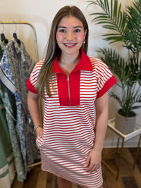 Woman wearing a red and white striped short sleeve dress with a zipper and collar neckline in a clothing store.