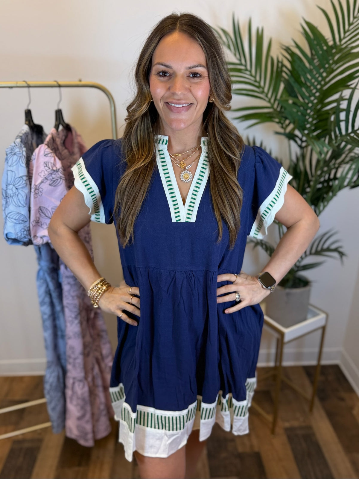 Woman wearing a blue dress with white and green trim details in a clothing store.