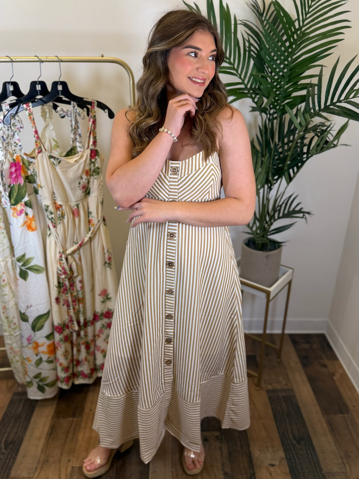 Woman wearing a striped dress standing in a room with clothing racks and plants.