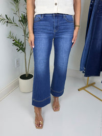 Person wearing blue wide leg jeans and heels with plant in back ground.