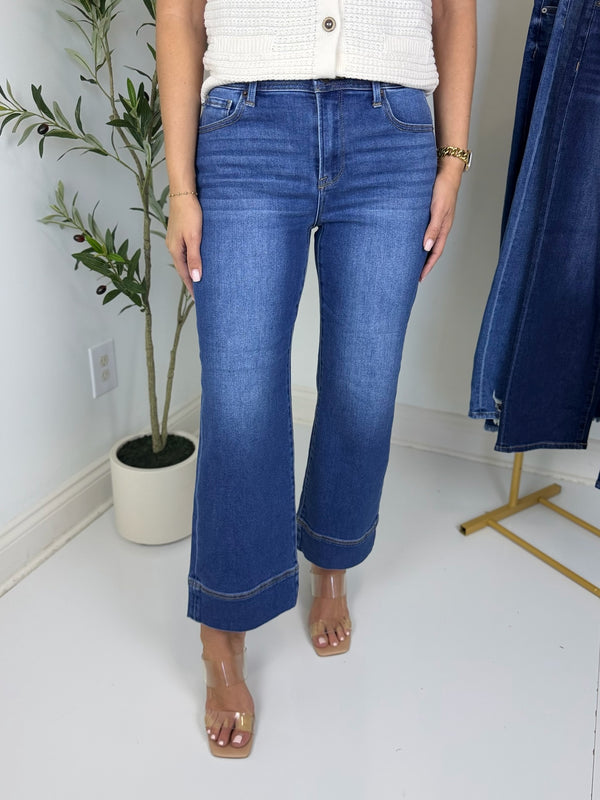 Person wearing blue wide leg jeans and heels with plant in back ground.