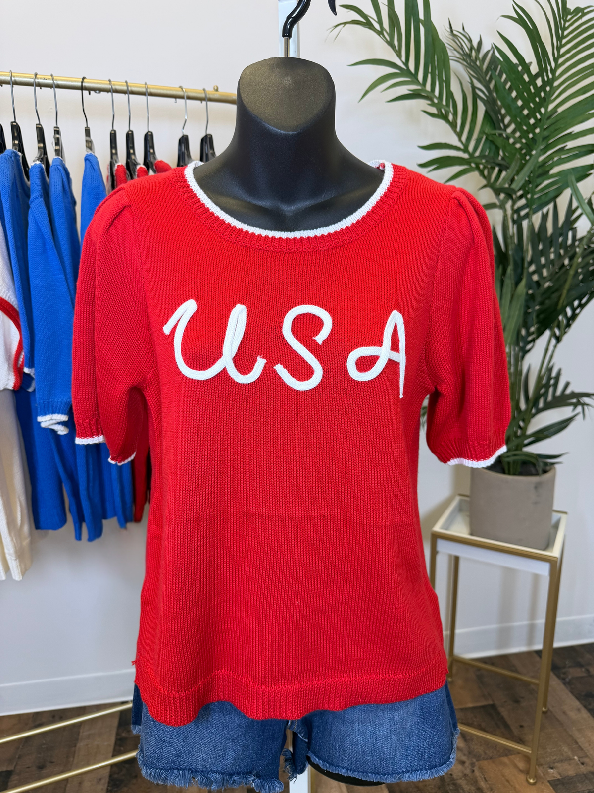 Red short sleeve sweater with 'USA' text on a mannequin in a store setting.