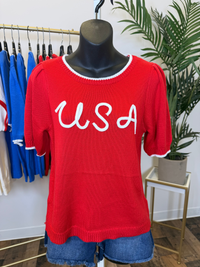 Red short sleeve sweater with 'USA' text on a mannequin in a store setting.