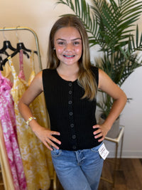 Young woman wearing a black sleeveless button-up knit top and blue jeans in a clothing store.