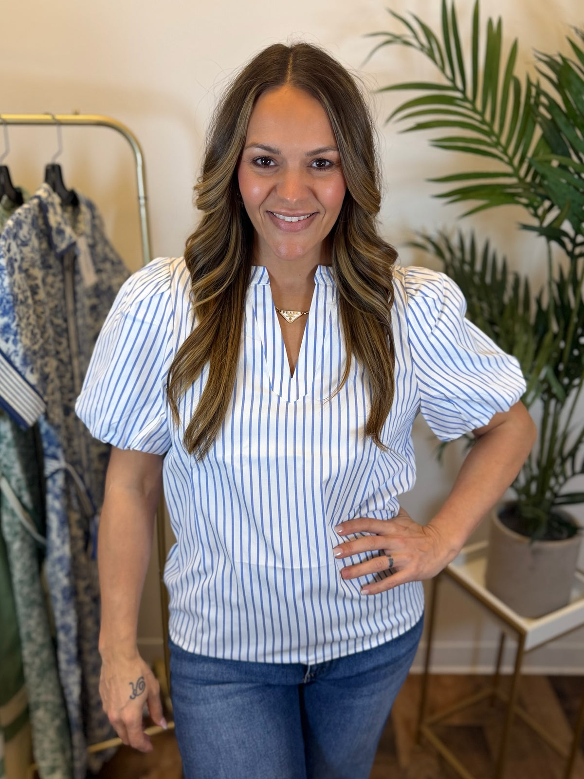 Woman wearing a blue and white striped blouse in a clothing store with plants in the background