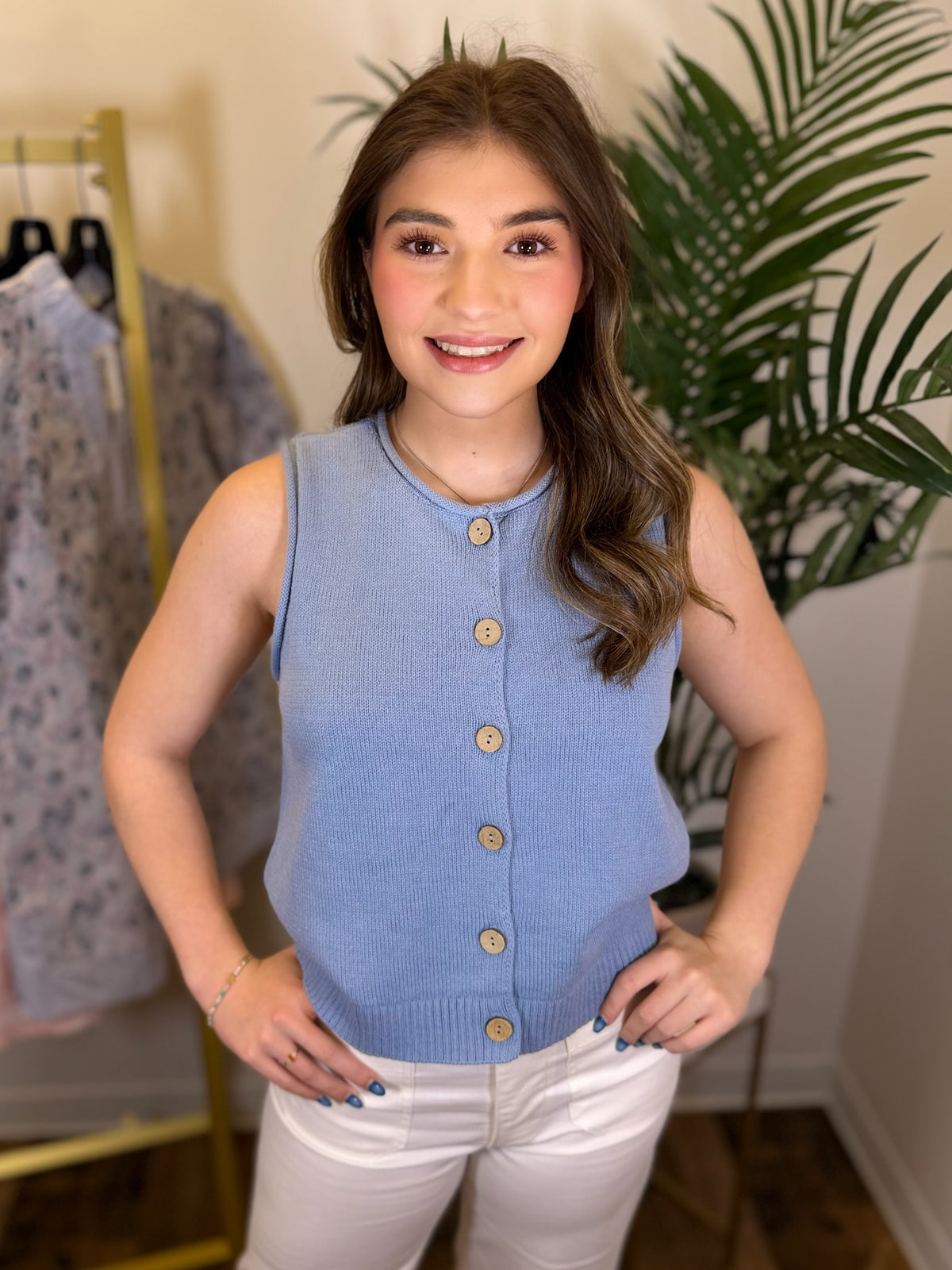 Woman wearing a blue sleeveless button-up top in a clothing store setting.
