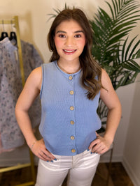 Woman wearing a blue sleeveless button-up top in a clothing store setting.