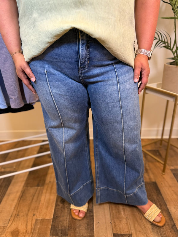Person wearing wide leg blue jeans and a light-colored top indoors.