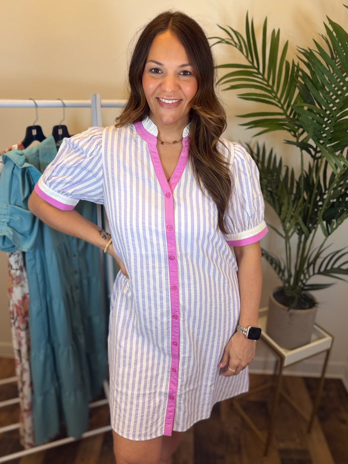 Woman wearing lavender and white striped dress with pink and white trim in clothing store setting.