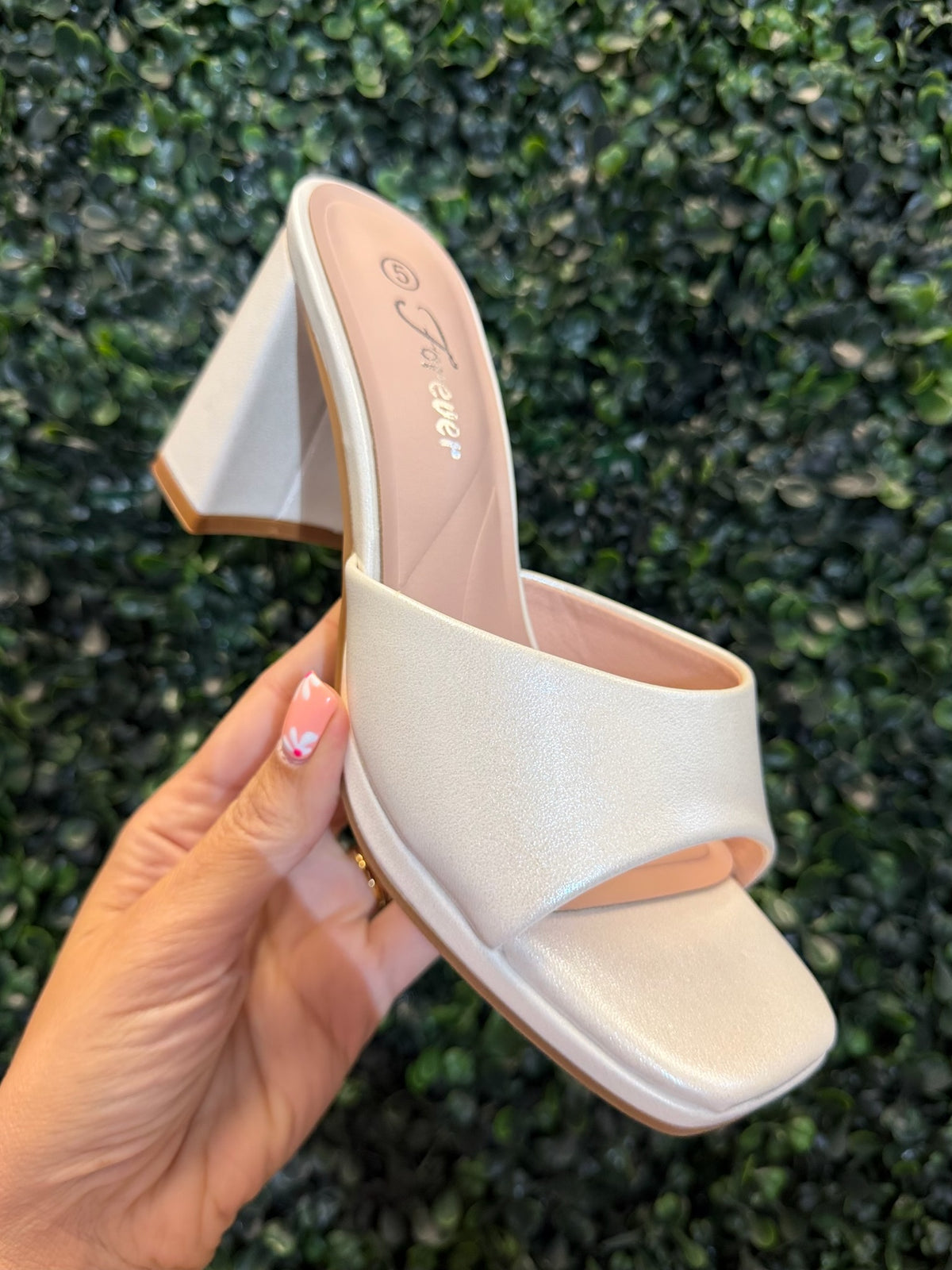 White block heel held by a hand against a green textured background