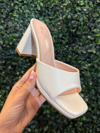 White block heel held by a hand against a green textured background
