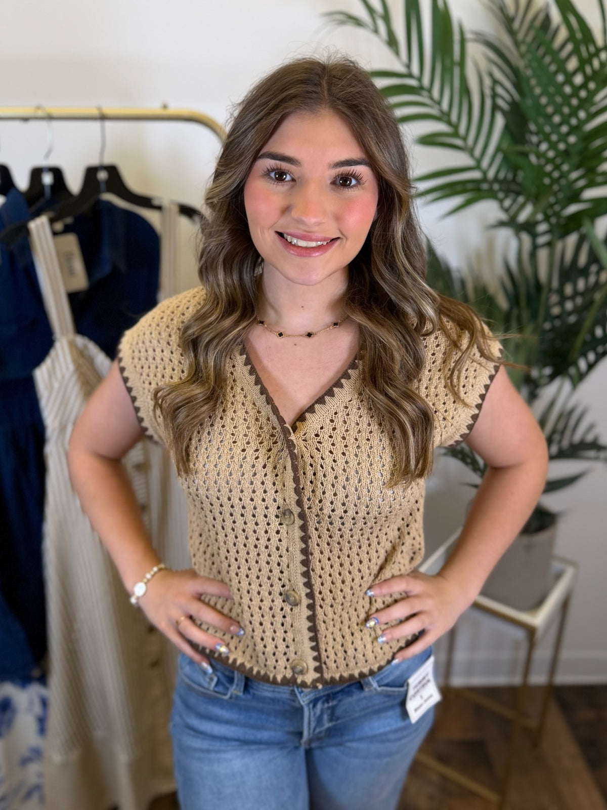 Woman wearing a beige crochet top and blue jeans in a clothing store.