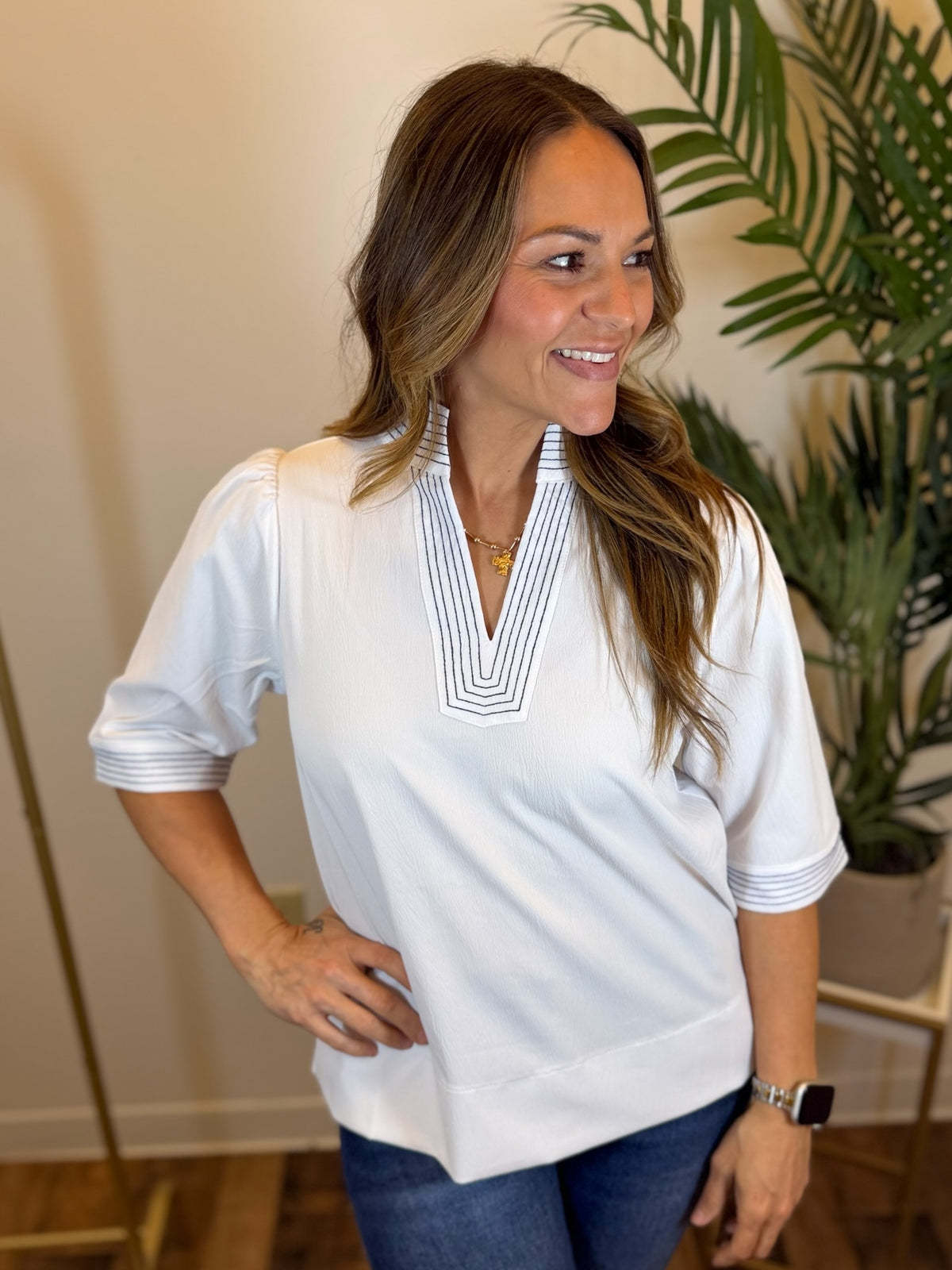 Woman wearing a white split neck blouse with a plant in the background