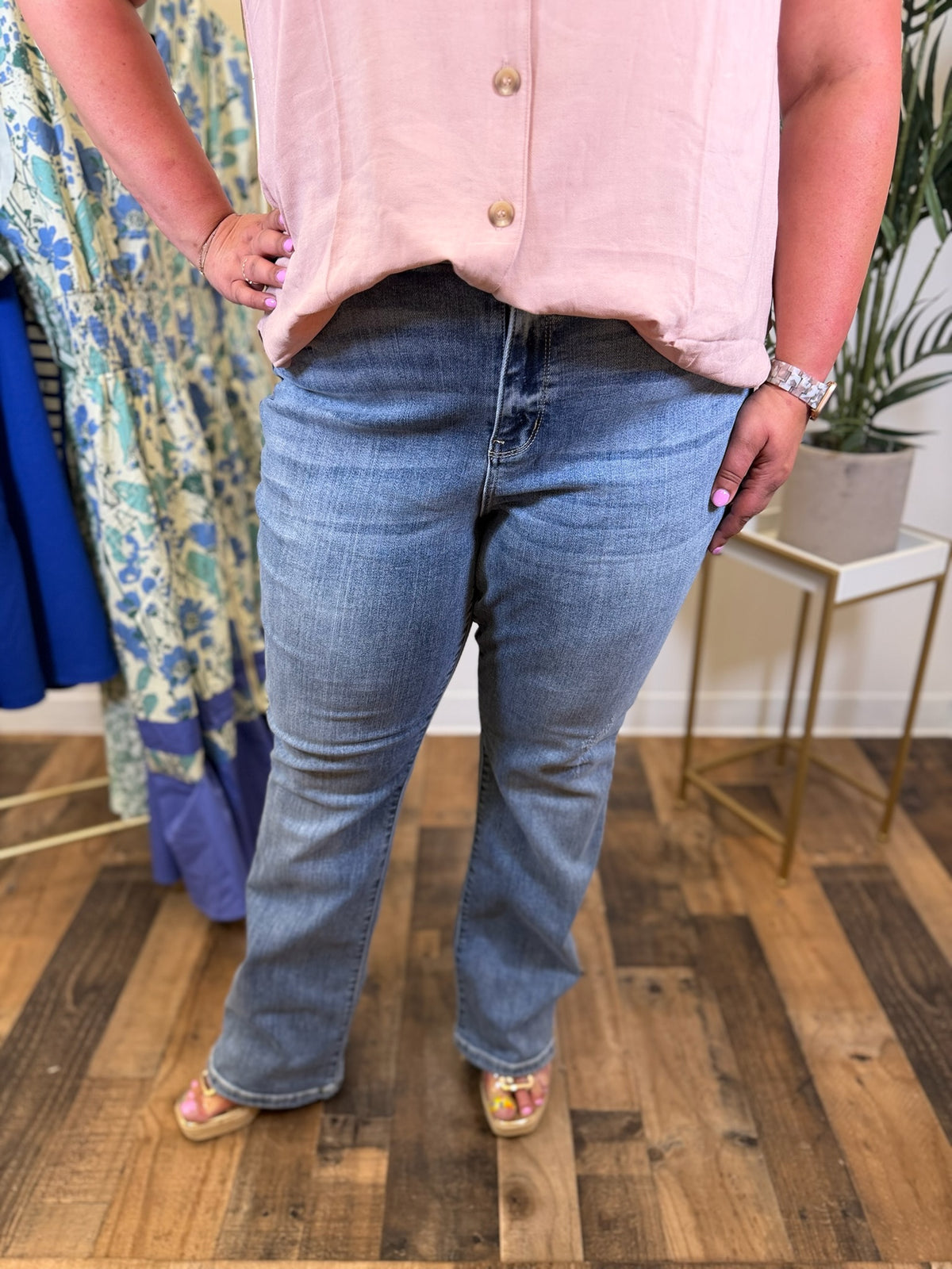 Person wearing medium wash bootcut blue jeans and a light pink button-up shirt in a store setting.