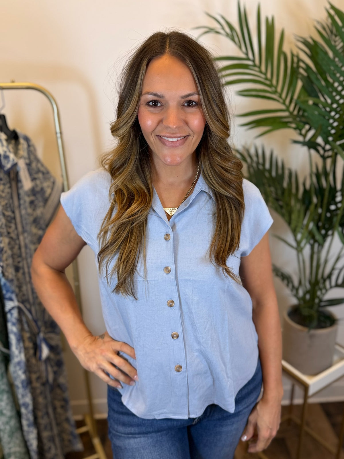 Woman wearing a light blue button-up shirt and jeans in a clothing store.