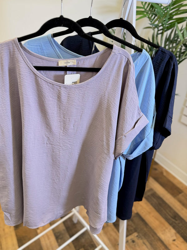 Lavender, light blue, and navy Easy Flow Everyday Tops with rolled sleeves on hangers.