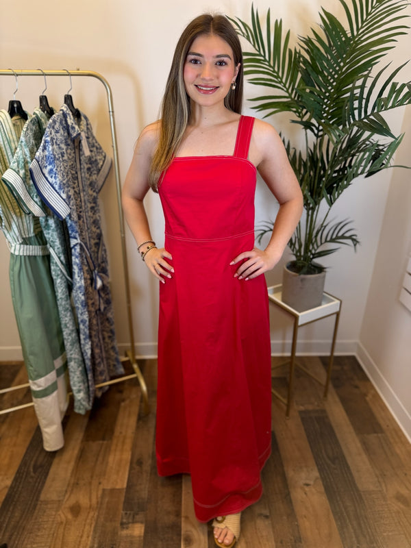 Woman in a red sleeveless dress with square neckline standing in a room with clothing racks and plants.