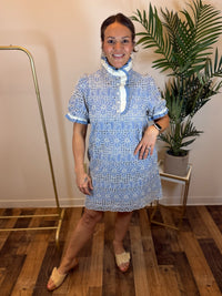 Woman wearing a periwinkle eyelet lace dress with puff sleeves and ruffled neckline standing indoors with a plant in the background