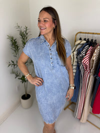 Woman wearing a blue mini dress standing in a room with a plant and clothing rack.