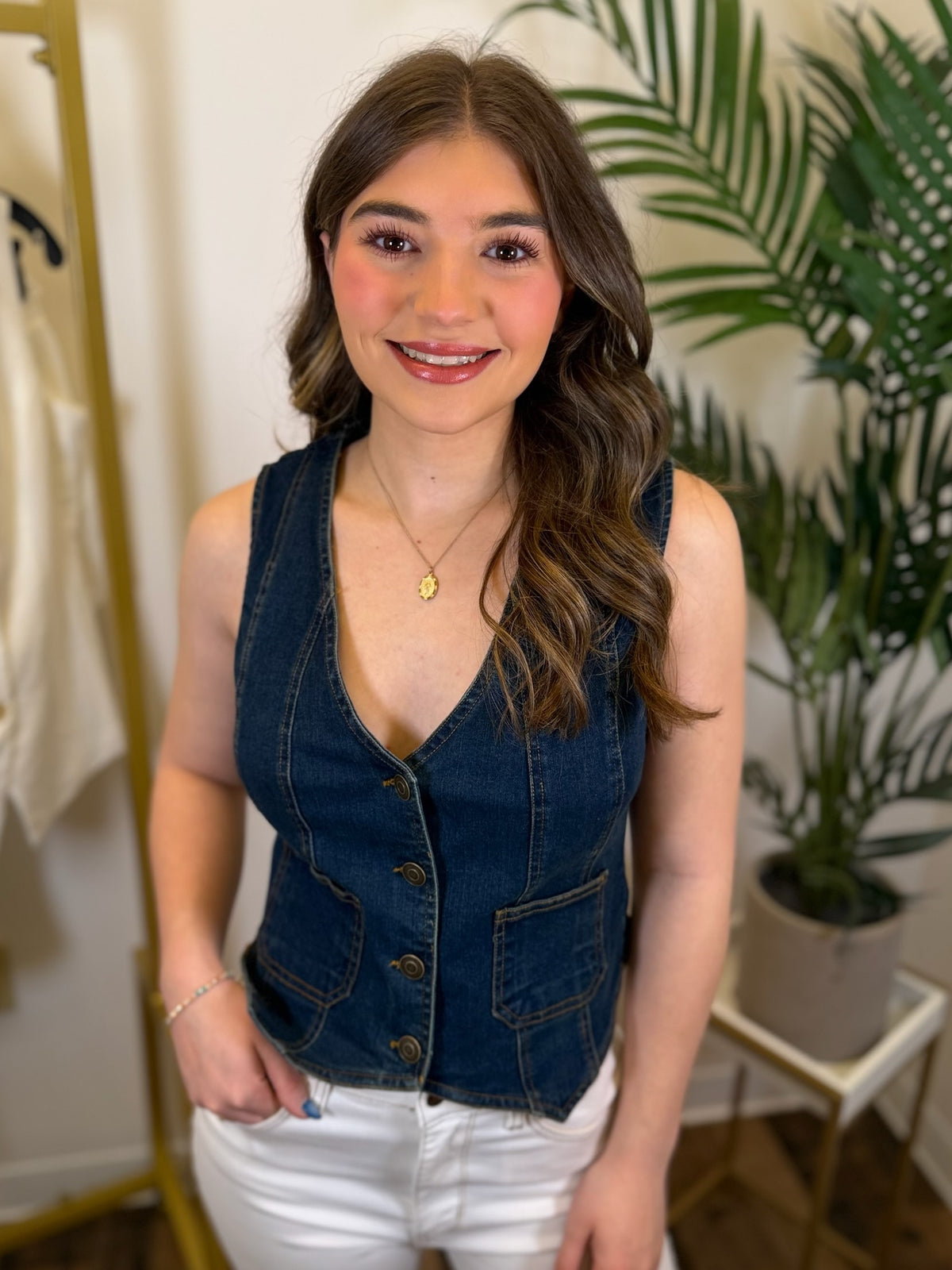 Woman wearing a denim vest and white pants in a room with plants and a rack.