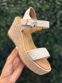 Beige sandal with woven sole held against a green leafy background