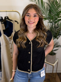 Woman wearing a black and tan short sleeve button front cardigan in a clothing store setting