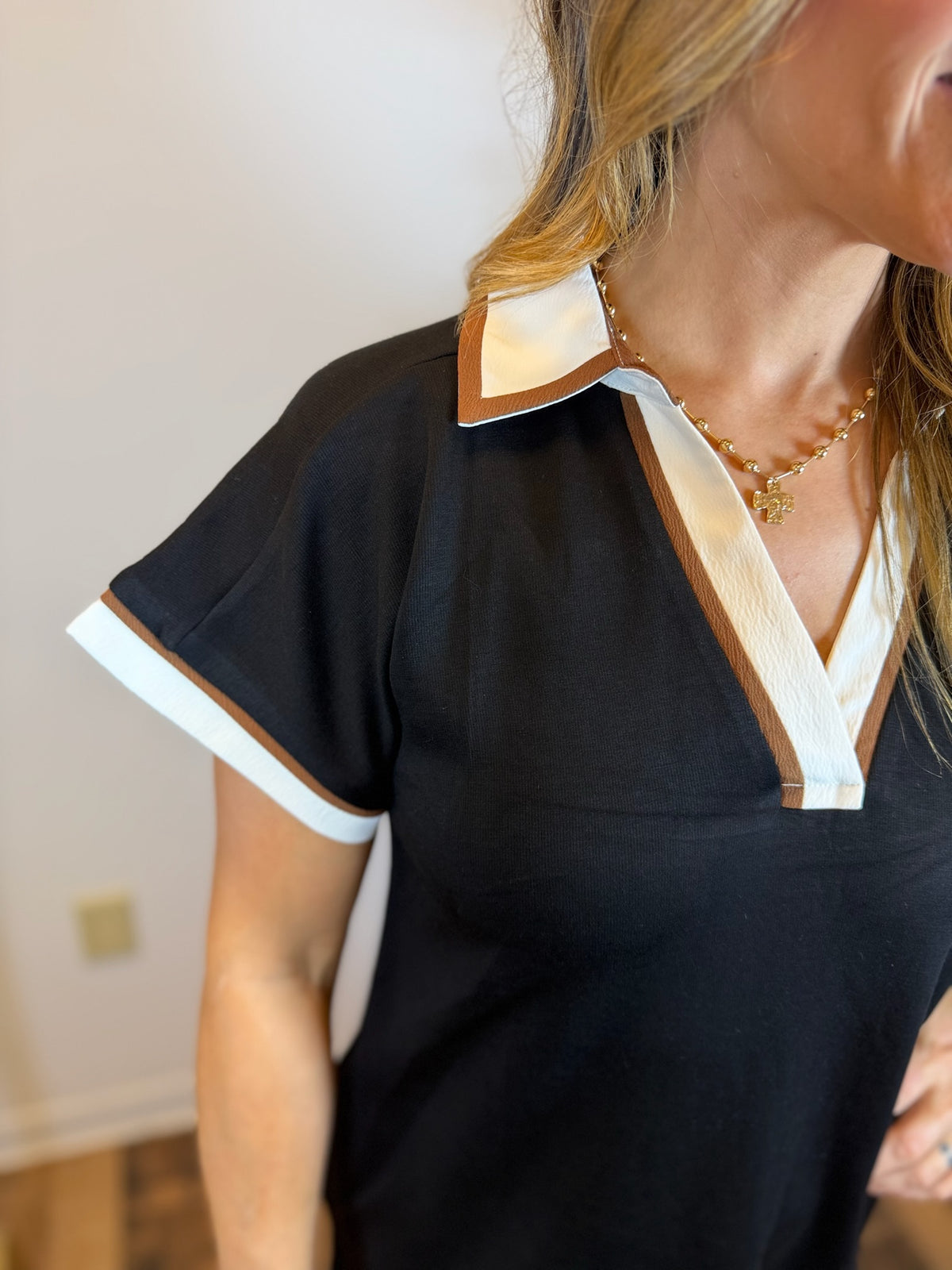Close up of woman wearing a black short sleeve dress with white and brown trim in an indoor setting