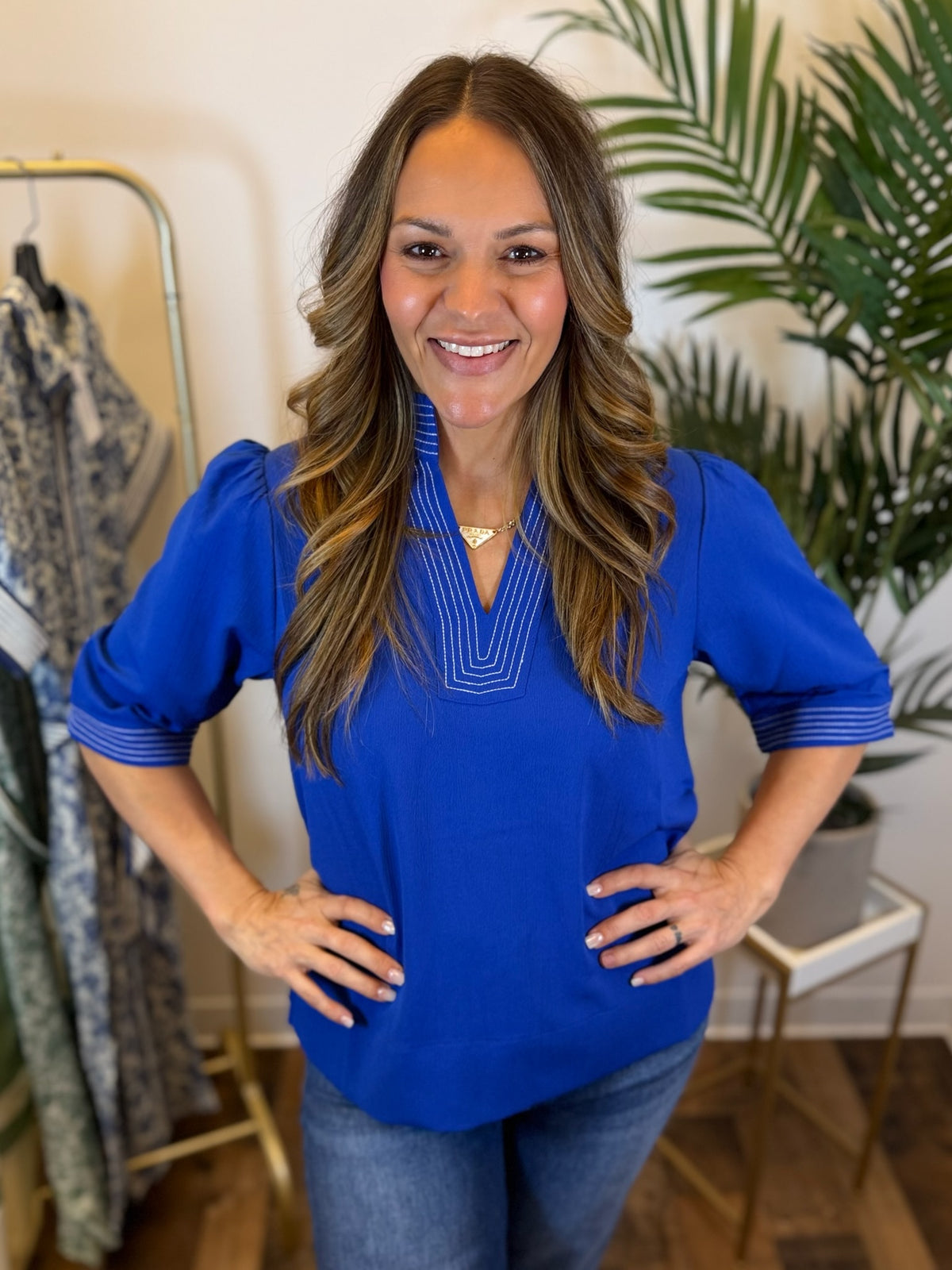 Woman wearing a royal blue blouse with split neckline and stitched trim details in a clothing store setting
