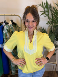 Woman wearing a yellow blouse with a striped collar in a clothing store.