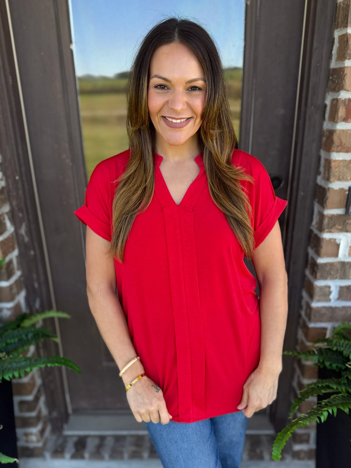 Woman wearing a red short sleeve blouse with a split V-neckline, standing outdoors.