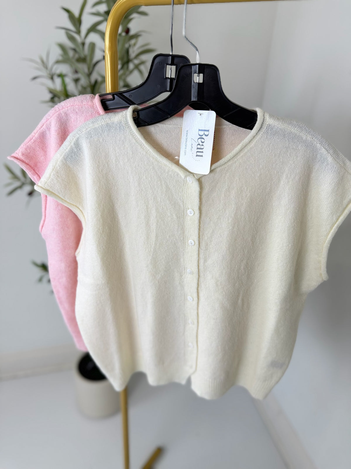Two cardigans, one pink and one beige, on hangers with a visible brand tag against a neutral background.