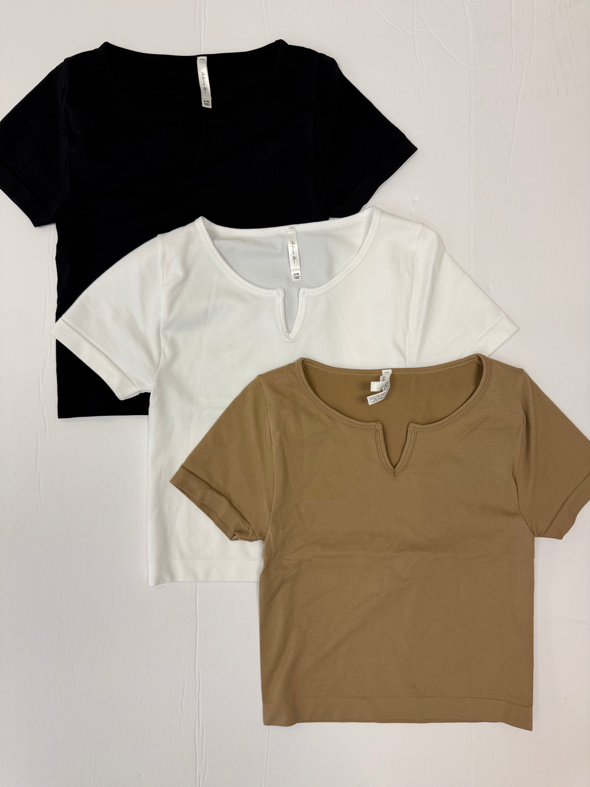 Three short sleeve crop tops with notched neckline in black, white, and mocha against a white background